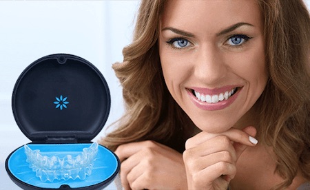 A beautiful smiling blond hair woman next to an Invisalign clear aligner case.