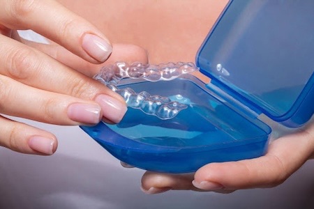 A Woman placing her Invisalign aligners in their plastic case.