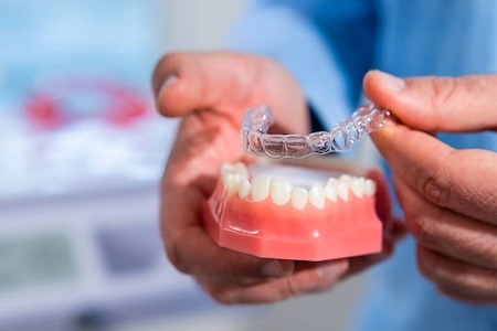 A male dentist is showing how to wear Invisalign clear aligners.