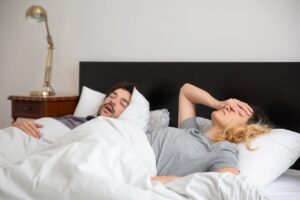 Couple in bed, one snoring, one frustrated