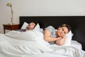 Couple in bed, one asleep, one awake