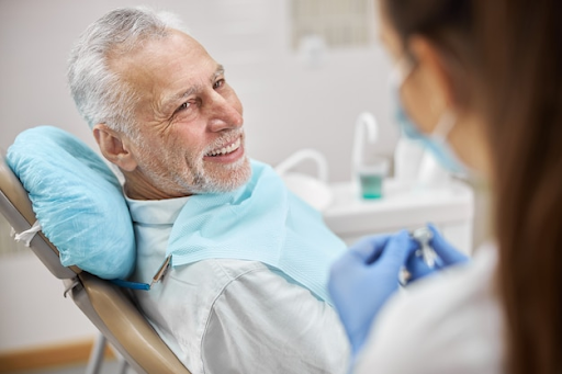Senior male patient undergoing dental consultation in a modern clinic, smiling during treatment discussion with dentist.