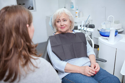 Senior female patient consulting with a full mouth rehabilitation dentist during a dental reconstruction cost consultation.