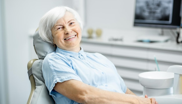 Smiling elderly patient sitting comfortably in a dental chair at a modern clinic, in an All on 4 dental implants cost consultation.